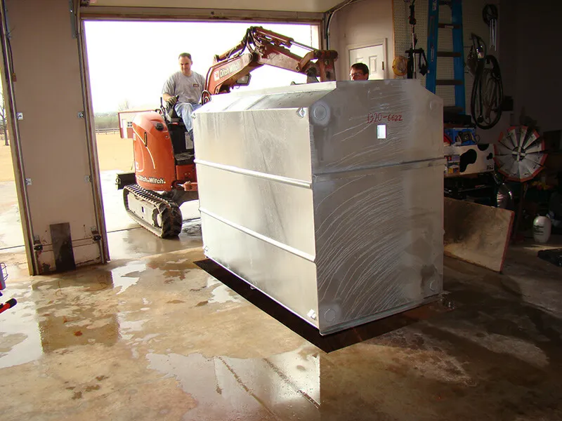 Heavy-duty galvanized underground storm shelter being lowered into a residential garage during professional installation in Oklahoma.