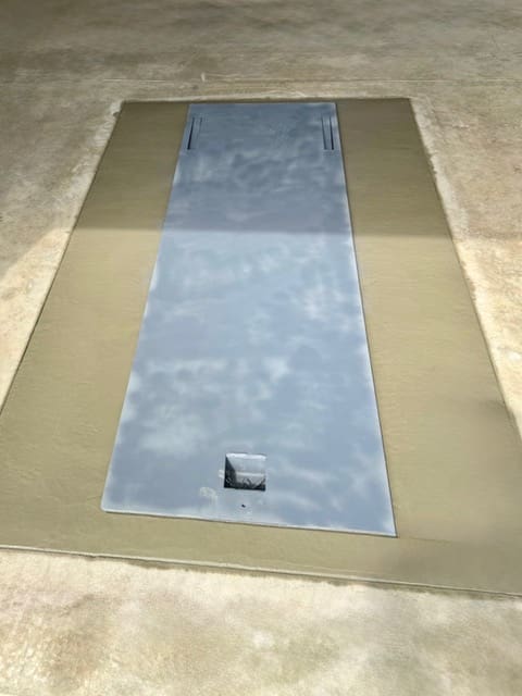Closed galvanized underground garage storm shelter with a flush-mounted steel door professionally installed beneath a residential concrete garage floor.