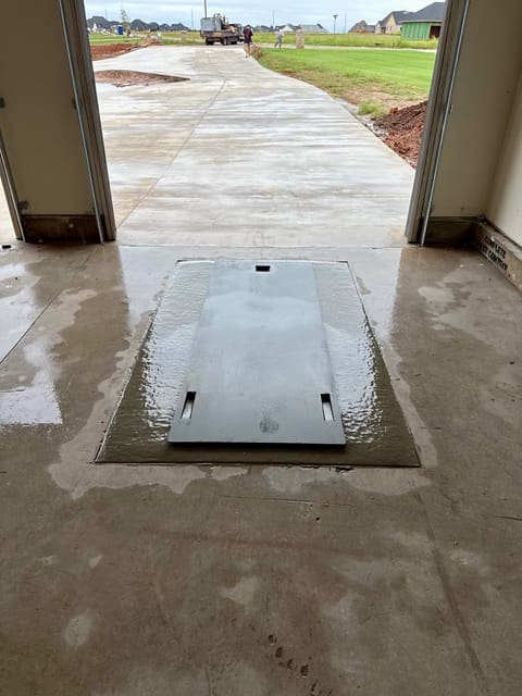 Closed galvanized underground garage storm shelter installed flush with a residential concrete garage floor in Oklahoma.