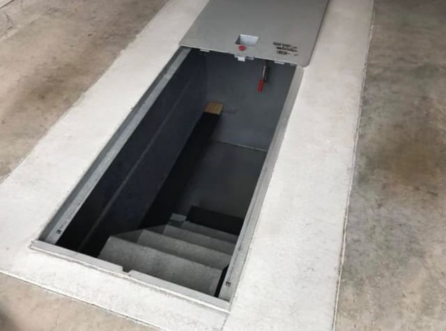 Open galvanized underground garage storm shelter with stairway entrance professionally installed beneath a residential concrete garage floor.