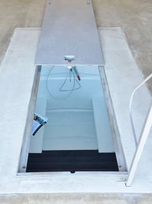 Open galvanized underground garage storm shelter with stairway entrance installed beneath a concrete garage floor in Oklahoma.