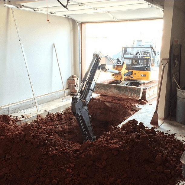 Excavator digging large hole inside garage